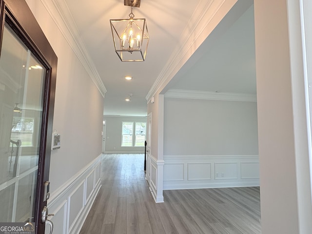 hall featuring crown molding, a chandelier, a wainscoted wall, wood finished floors, and a decorative wall