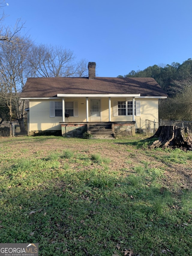 rear view of house with a porch, a chimney, a yard, and fence