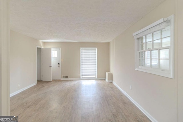 empty room featuring visible vents, plenty of natural light, a textured ceiling, and light wood-style floors