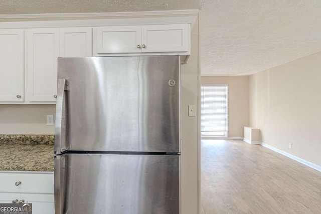 kitchen with white cabinetry, baseboards, light wood-style flooring, freestanding refrigerator, and a textured ceiling