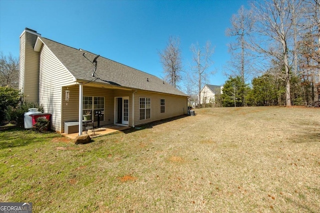 back of house featuring a lawn, a shingled roof, a chimney, and a patio area