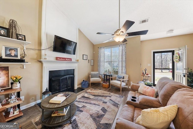 living area featuring visible vents, a fireplace with flush hearth, wood finished floors, and vaulted ceiling