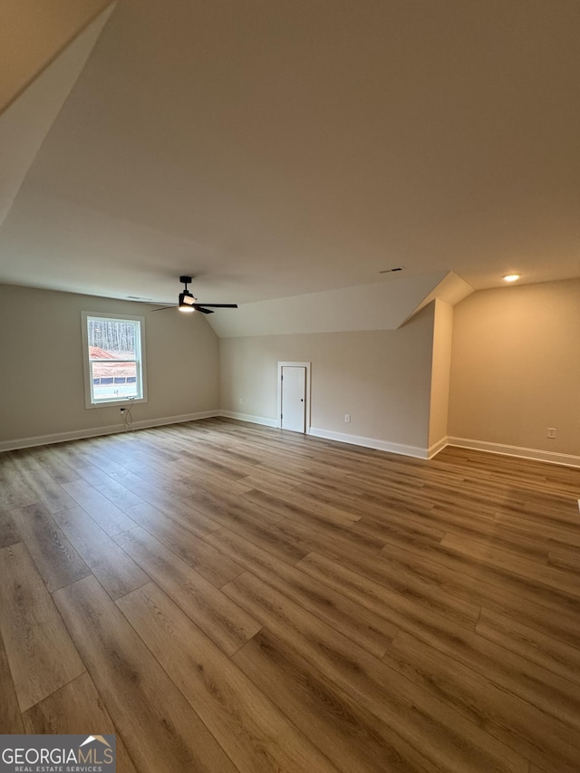 empty room with a ceiling fan, lofted ceiling, wood finished floors, and baseboards