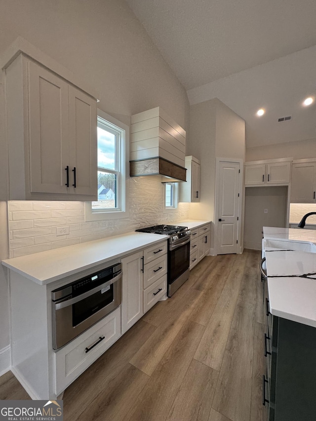 kitchen with visible vents, premium range hood, light wood finished floors, stainless steel appliances, and vaulted ceiling