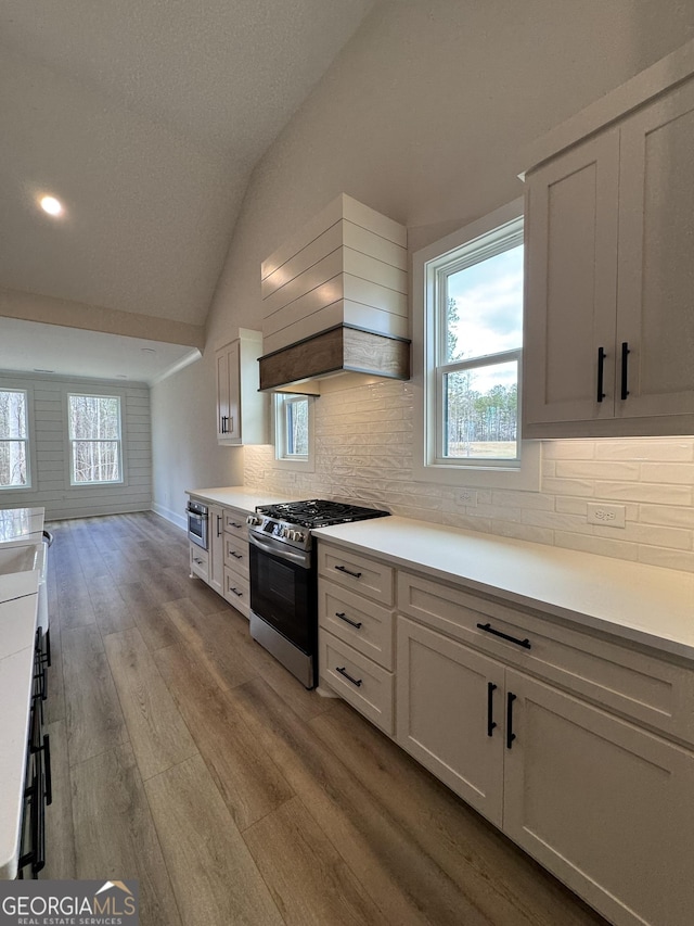 kitchen featuring wood finished floors, lofted ceiling, decorative backsplash, custom range hood, and stainless steel gas range oven