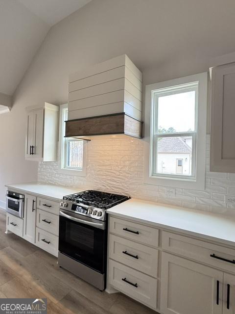 kitchen featuring lofted ceiling, light wood-style flooring, custom exhaust hood, white cabinets, and appliances with stainless steel finishes