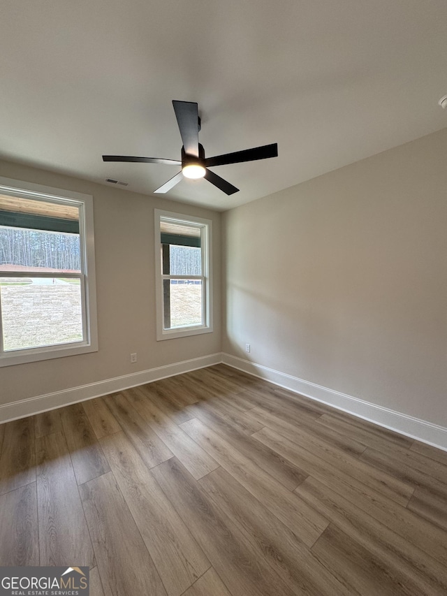 unfurnished room featuring ceiling fan, visible vents, baseboards, and dark wood finished floors