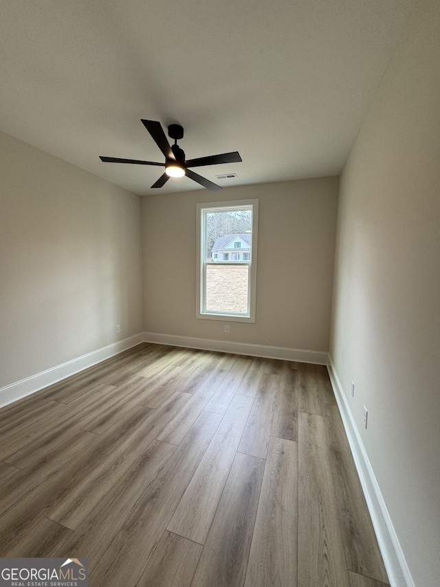 empty room featuring visible vents, a ceiling fan, baseboards, and wood finished floors