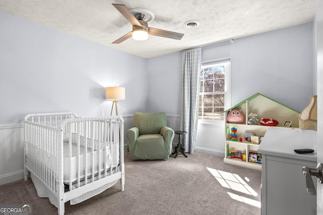 bedroom with visible vents, ceiling fan, carpet flooring, a textured ceiling, and a nursery area