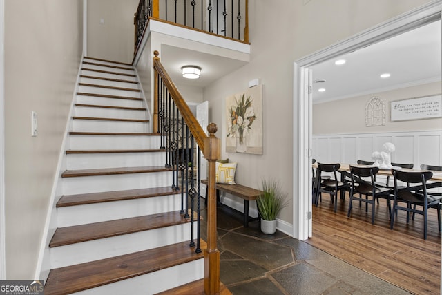 staircase featuring wood finished floors, recessed lighting, crown molding, a decorative wall, and baseboards