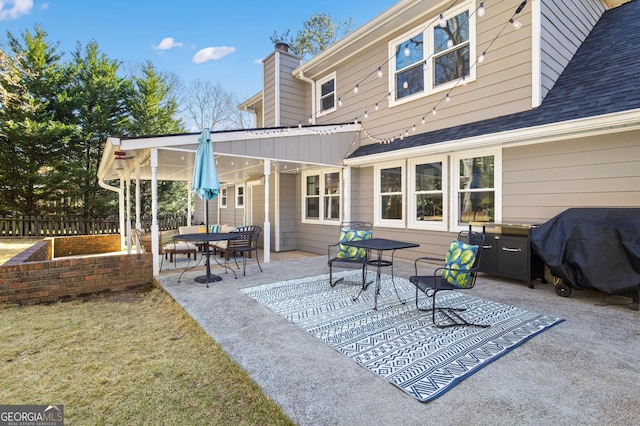 rear view of property with a chimney, a patio area, fence, and a shingled roof