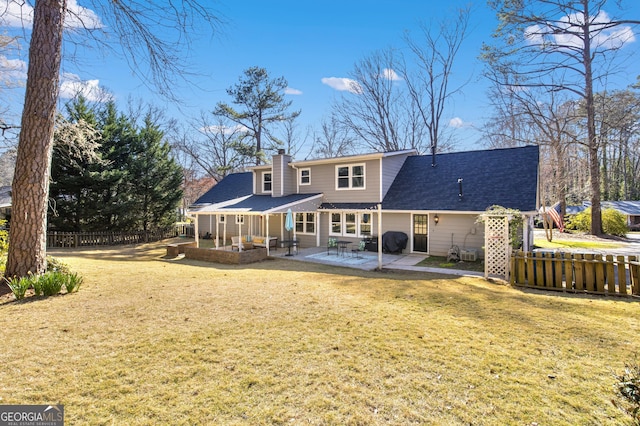 rear view of house with fence, roof with shingles, a lawn, a chimney, and a patio