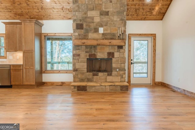 unfurnished living room with plenty of natural light, a stone fireplace, light wood-style flooring, and vaulted ceiling