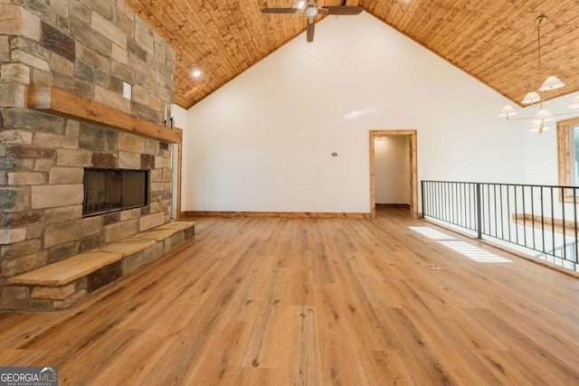 unfurnished living room with high vaulted ceiling, wood finished floors, a stone fireplace, wooden ceiling, and baseboards