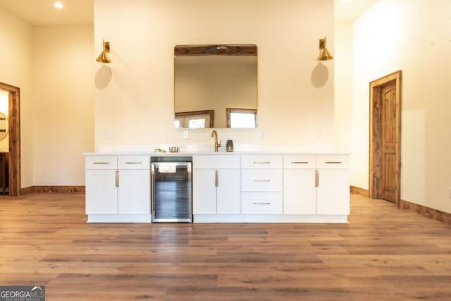 kitchen featuring beverage cooler, a sink, light countertops, white cabinets, and light wood-type flooring