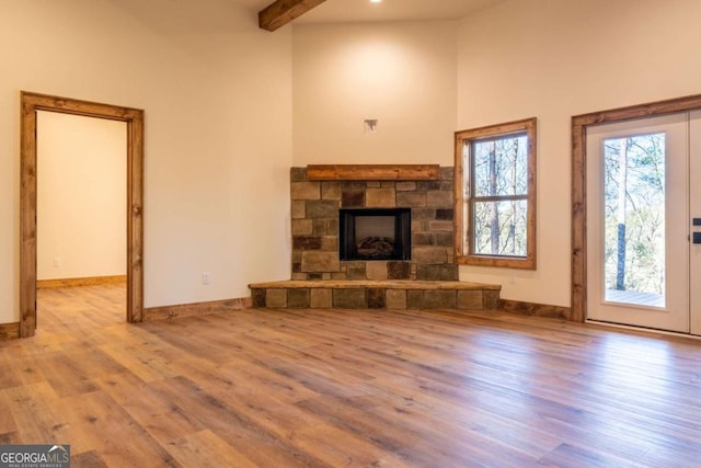 unfurnished living room with a stone fireplace, beamed ceiling, baseboards, and wood finished floors