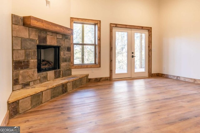 unfurnished living room with a stone fireplace, wood finished floors, plenty of natural light, and french doors