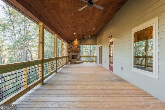 deck featuring an outdoor stone fireplace and a ceiling fan