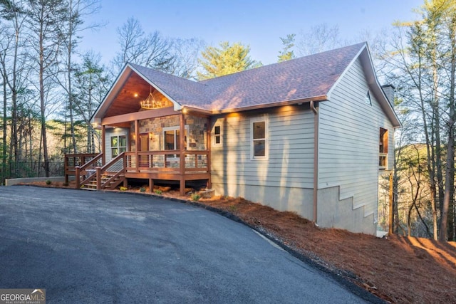 chalet / cabin with stone siding, roof with shingles, and a deck