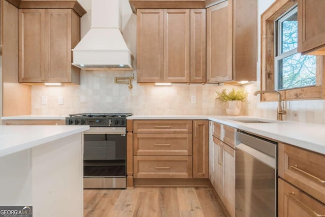 kitchen featuring light wood-style flooring, a sink, appliances with stainless steel finishes, light countertops, and custom exhaust hood