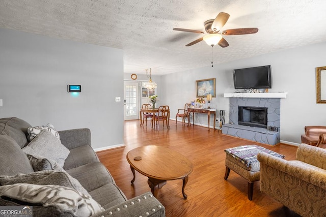 living room with a fireplace, a textured ceiling, a ceiling fan, and wood finished floors