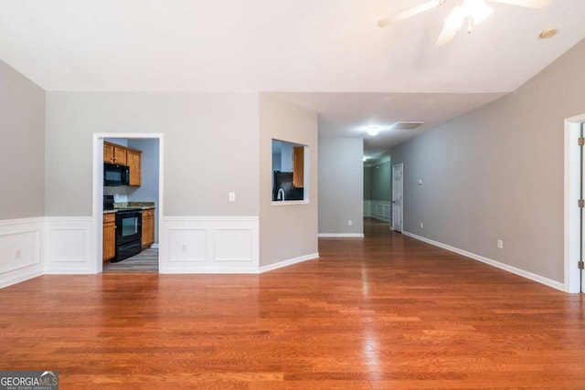 unfurnished living room with a decorative wall, wood finished floors, wainscoting, and ceiling fan