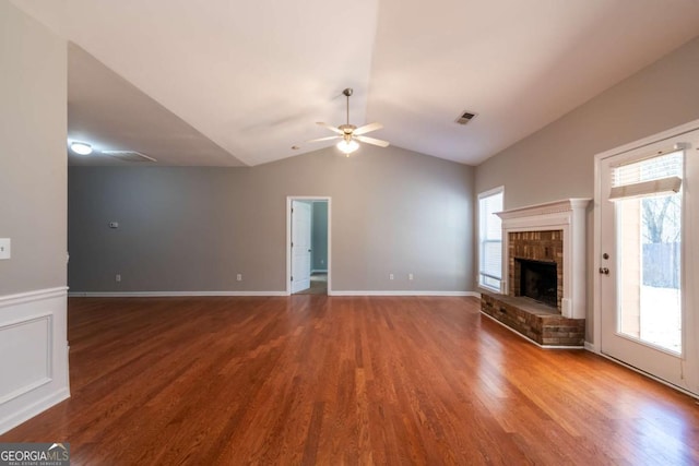 unfurnished living room with visible vents, wood finished floors, a fireplace, ceiling fan, and vaulted ceiling