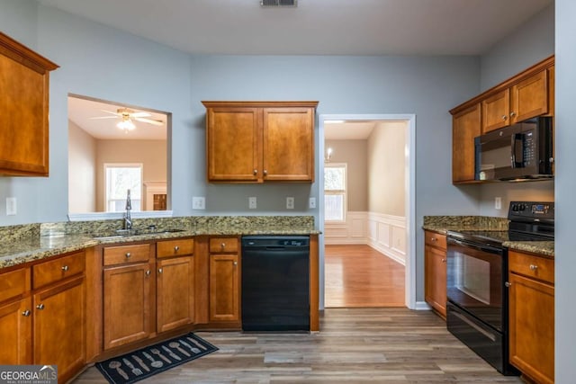 kitchen with a sink, light wood-type flooring, black appliances, and brown cabinetry