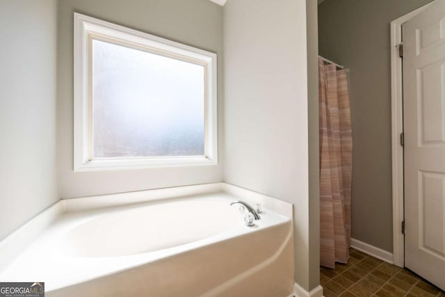 bathroom featuring a shower with shower curtain, a bath, and baseboards