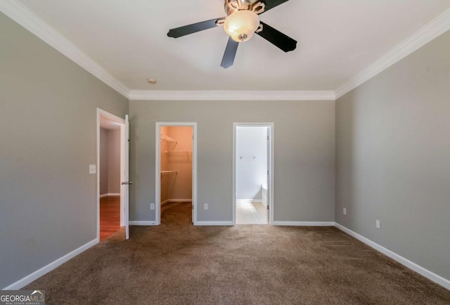 unfurnished bedroom featuring carpet flooring, baseboards, a spacious closet, and crown molding