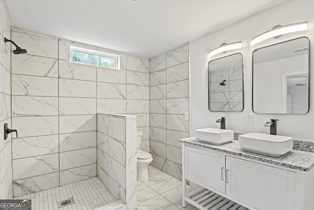 bathroom featuring double vanity, tiled shower, marble finish floor, and a sink