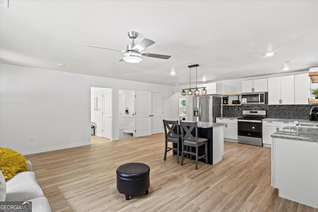 kitchen with a kitchen island, white cabinetry, stainless steel appliances, light wood-style floors, and decorative backsplash