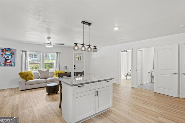 kitchen with light wood finished floors, a center island, open floor plan, light stone counters, and white cabinetry