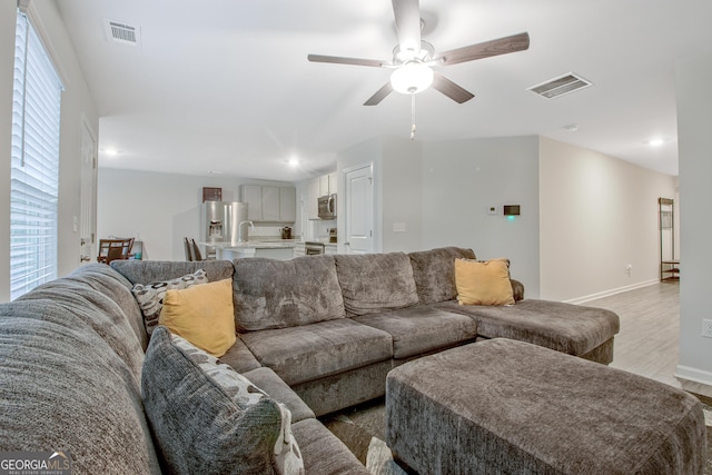 living area with visible vents, baseboards, a ceiling fan, and light wood finished floors