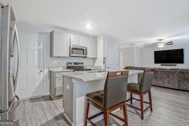 kitchen featuring a kitchen bar, light stone countertops, light wood-style floors, and appliances with stainless steel finishes