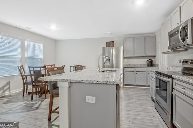 kitchen featuring a kitchen island with sink, a sink, light wood-style floors, appliances with stainless steel finishes, and a kitchen breakfast bar