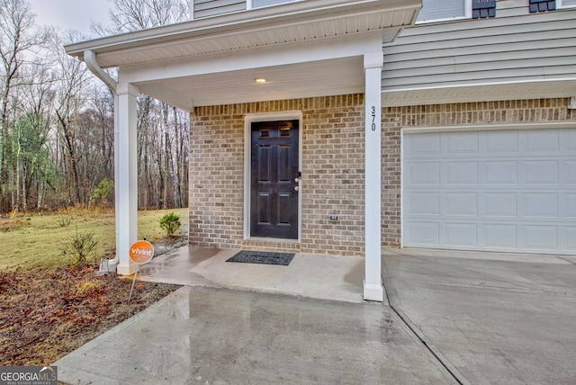 entrance to property featuring a garage, brick siding, and concrete driveway