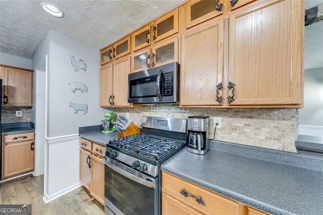 kitchen with light wood-type flooring, light brown cabinets, dark countertops, appliances with stainless steel finishes, and decorative backsplash