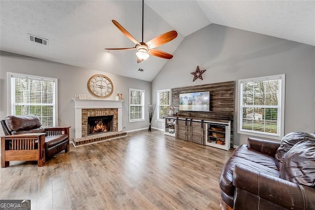 living room with a ceiling fan, wood finished floors, visible vents, a healthy amount of sunlight, and a fireplace