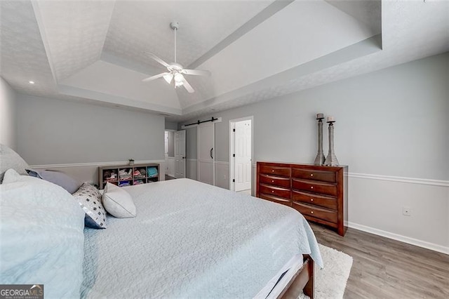 bedroom featuring a ceiling fan, a raised ceiling, baseboards, and wood finished floors