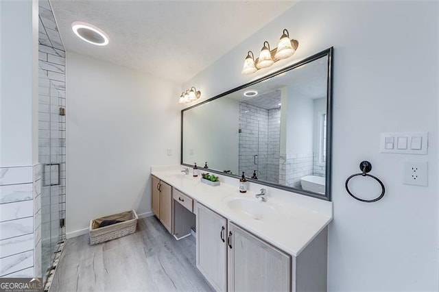 full bathroom with a sink, double vanity, wood finished floors, and a shower stall