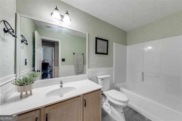 full bath with a wainscoted wall, toilet, vanity, and a textured wall