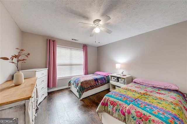 bedroom featuring dark wood-style floors, visible vents, a textured ceiling, and a ceiling fan