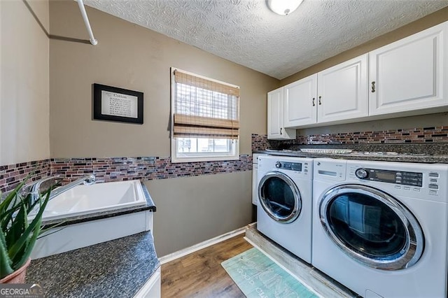 clothes washing area with washer and dryer, a sink, a textured ceiling, wood finished floors, and cabinet space