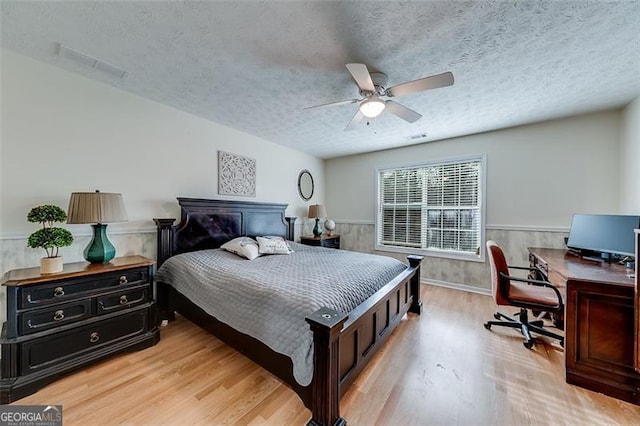 bedroom with a wainscoted wall, a textured ceiling, and light wood finished floors