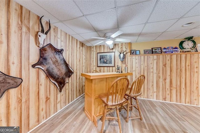 bar with ceiling fan, wood walls, a dry bar, wood finished floors, and a paneled ceiling