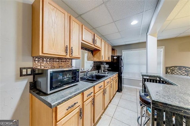 kitchen featuring stainless steel microwave, light brown cabinets, baseboards, light tile patterned flooring, and a sink