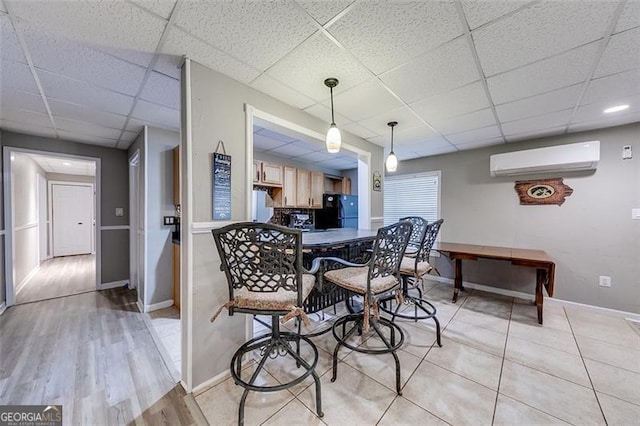 dining room featuring a drop ceiling, baseboards, light wood-style floors, and a wall mounted AC