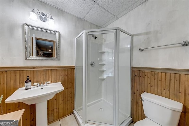 full bathroom with a drop ceiling, a shower stall, wood walls, wainscoting, and toilet