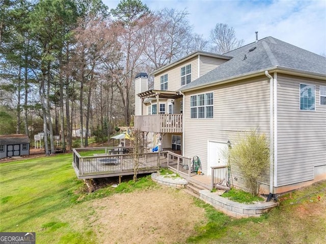 back of property featuring an outbuilding, a deck, a lawn, and roof with shingles